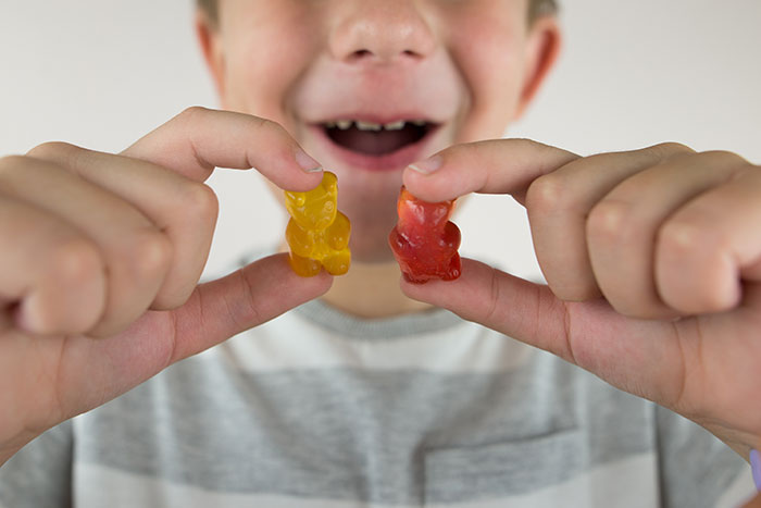 Child holding two gummy bears between fingers, illustrating people who tried DIY medical treatments that went wrong.