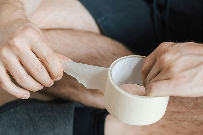 Person tearing medical tape while attempting DIY medical treatment, illustrating risks of failed self-care attempts.
