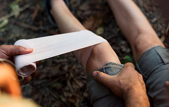 Person applying a bandage to their knee outdoors, illustrating DIY medical treatments that went wrong.