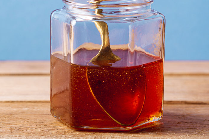 Close-up of a jar with a golden spoon stirring thick amber liquid, illustrating DIY medical treatments gone wrong.