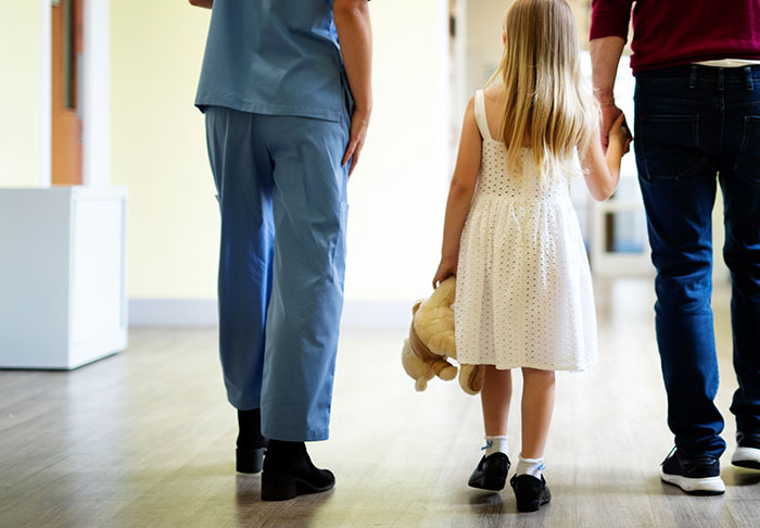 Child holding a teddy bear walking with an adult and a medical professional showing the risks of DIY medical treatments.