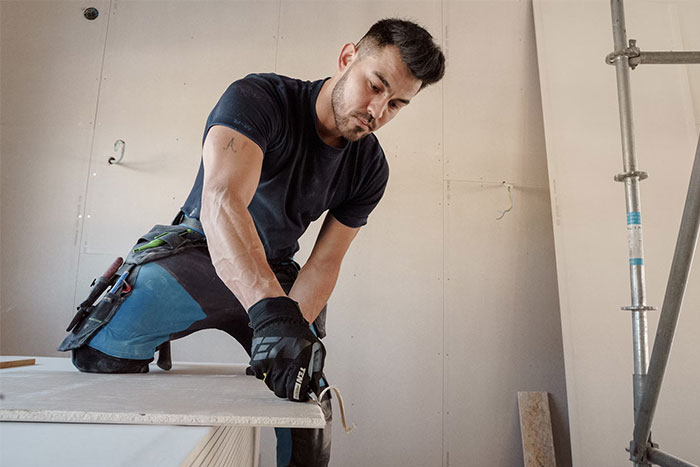 Man working in a stranger’s home, using a tool to cut material, showcasing people who work in strangers’ homes.
