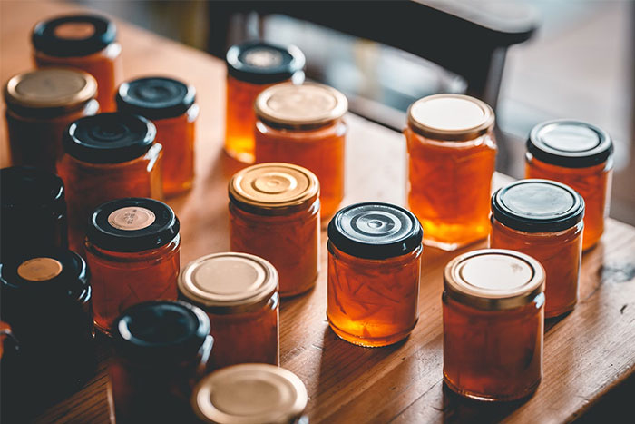Jars of homemade preserves on a wooden table, representing unique things seen inside strangers’ homes.