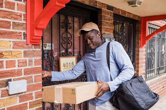 Delivery worker at a stranger’s home holding a package, illustrating experiences of people who work in strangers’ homes.