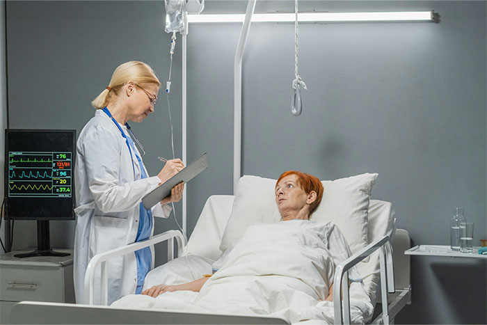 Healthcare professional working in a stranger’s home, interacting with a patient in a hospital bed with medical equipment nearby.