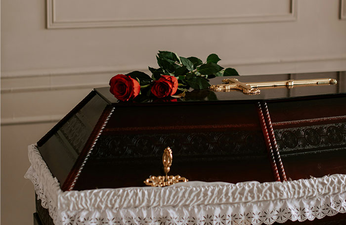 Dark wooden coffin with gold cross and two red roses on top, reflecting unforgettable things seen inside strangers’ homes.
