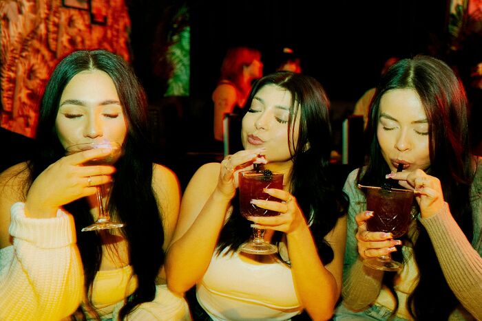 Three women enjoying cocktails at a bar, highlighting bartender stories beyond just pouring drinks.