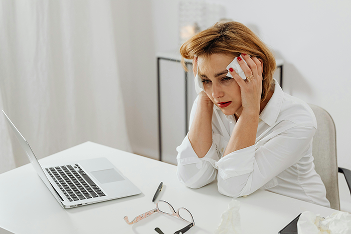 Stressed woman in office holding tissue to her face, showing tears and drama during a tense workday at the 9-to-5 job.