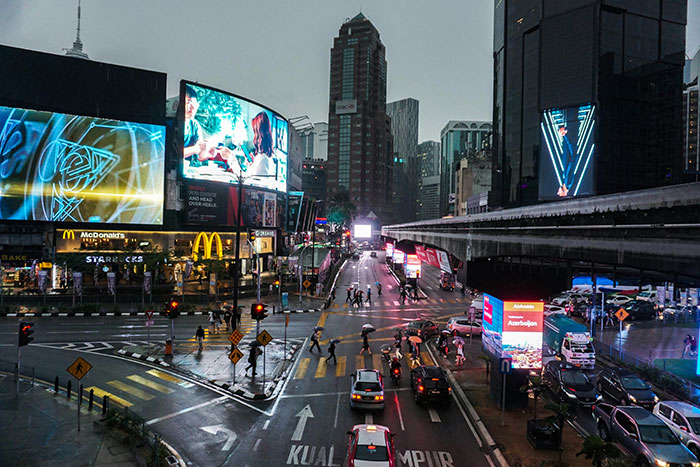 Busy city street at dusk with pedestrians crossing and vibrant digital billboards, illustrating cultural differences worldwide.