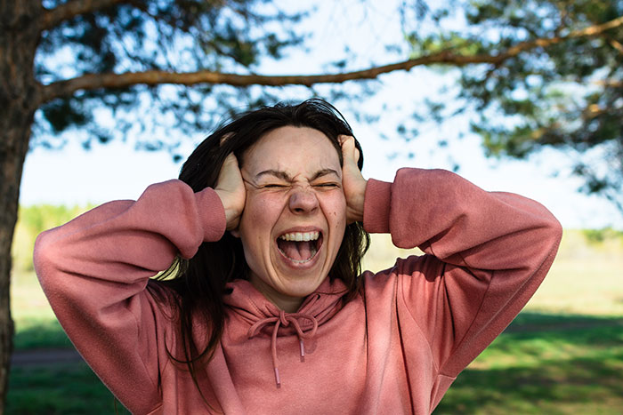 Young woman in a pink hoodie outdoors expressing frustration illustrating mind-blowing cultural differences in reactions and emotions.