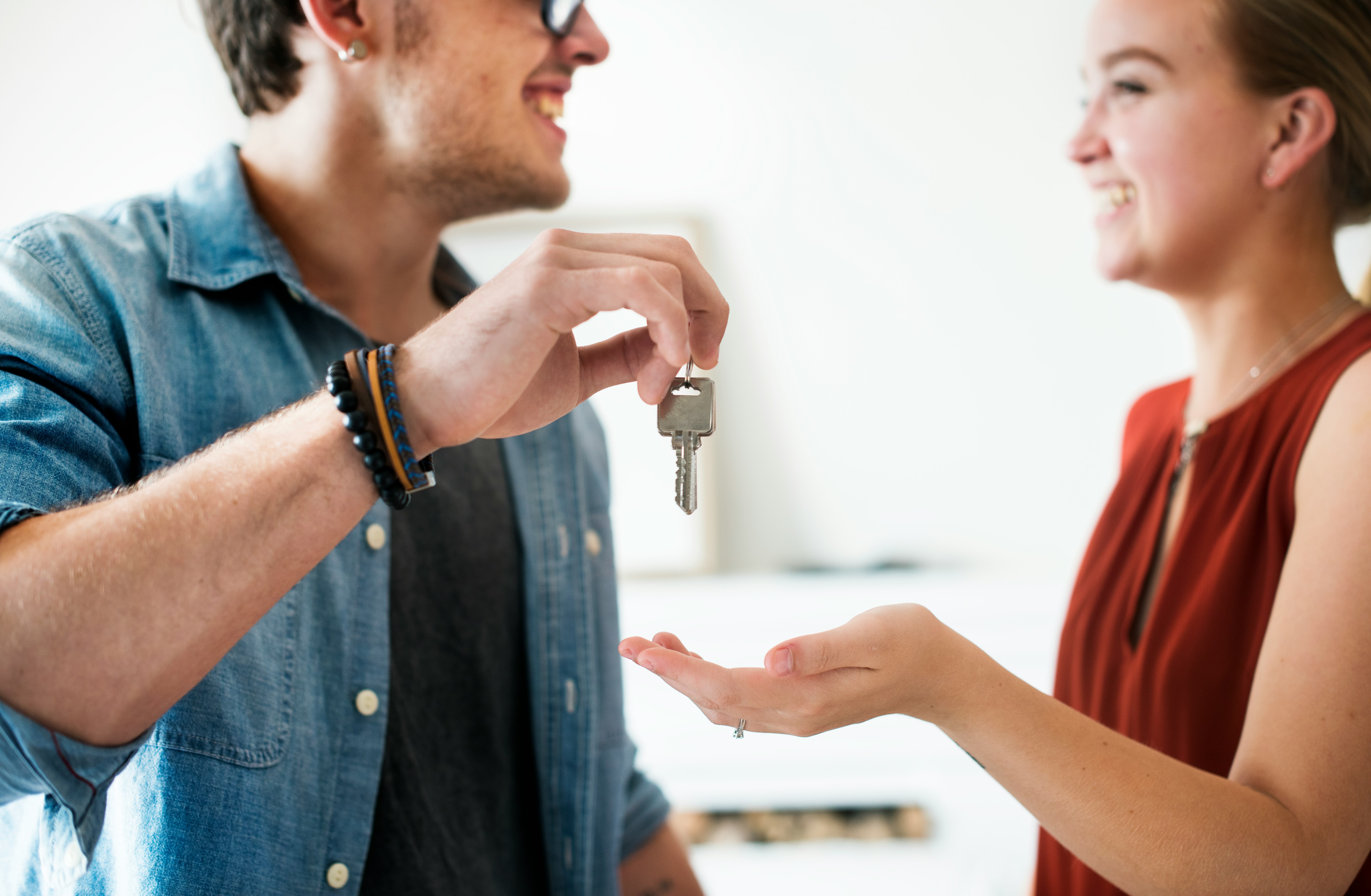 Man handing house key to woman, both smiling, representing husband unsure how to come clean about a lie from years ago.