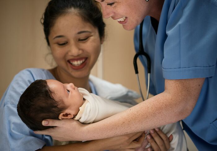Smiling nurse and mother holding newborn baby wrapped in blanket during a joyful hospital moment about baby names.