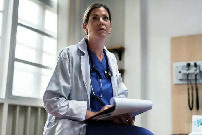 Female doctor in a white coat with stethoscope holding notes, reflecting on company secret shared after leaving job.