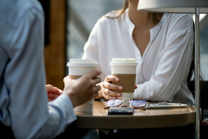 Two people holding takeaway coffee cups, sitting at a table discussing small decisions that changed life forever.