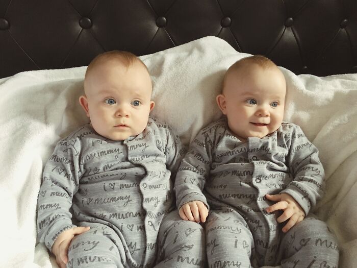 Two babies in matching gray pajamas sitting on a white blanket, illustrating hilariously bad baby names concept.