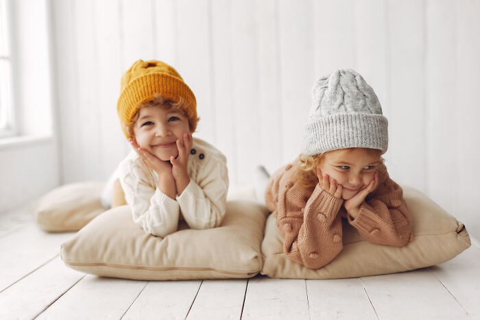 Two young children wearing knitted hats and sweaters, lying on cushions, evoking hilariously bad names concept.