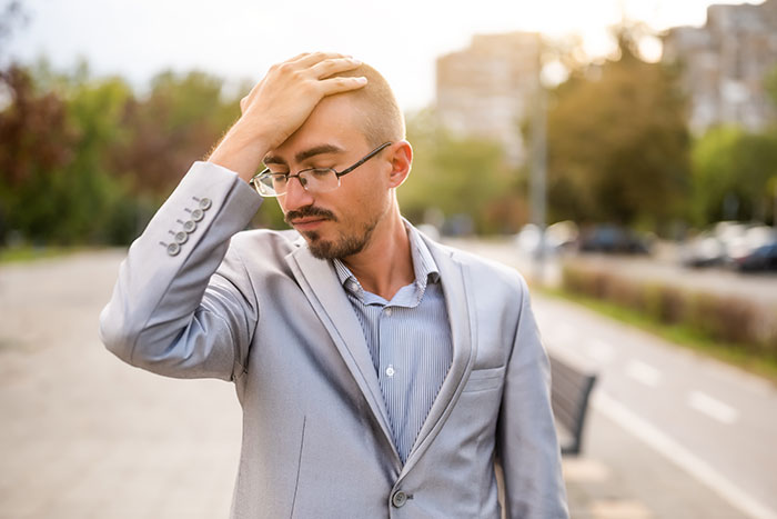 Young man in a suit outside, looking frustrated after trying to get a job at a physical office with his dad.