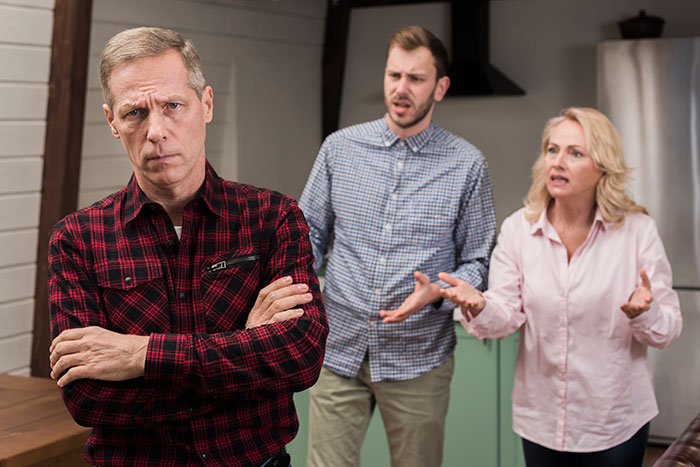 Man prioritizing his miniature wargaming studio, standing arms crossed while daughter and fianc&eacute; argue in the background.