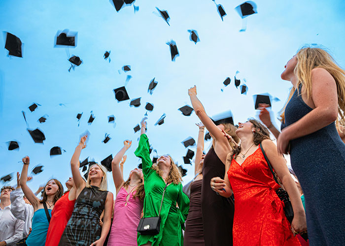 Teenagers celebrating graduation by throwing caps in the air, capturing the moment of a graduation event.
