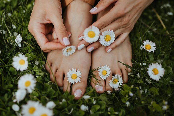 Hands placing daisies on toes surrounded by grass, illustrating unusual and weirdest ways to earn quick money.