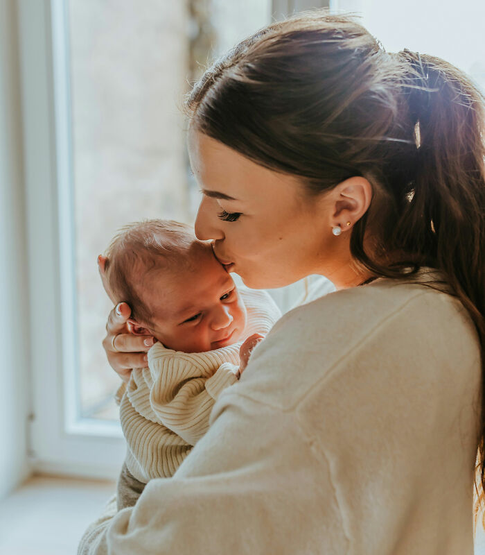 Mother holding and kissing newborn baby, illustrating hilariously bad names that had people questioning parenting choices.