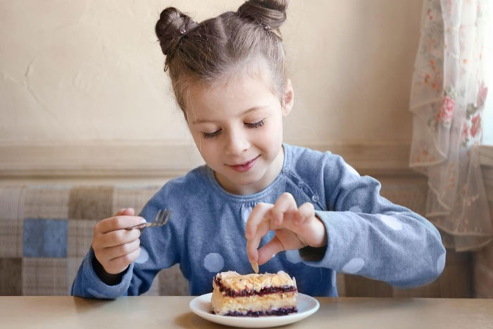 Young girl in blue shirt eating cake, highlighting confusion over eggs as dairy in dairy-free desserts debate.
