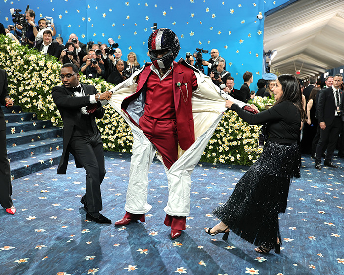 Damson Idris stuns at Met Gala 2025 with dramatic reveal beneath F1 racing suit on blue carpet with photographers.