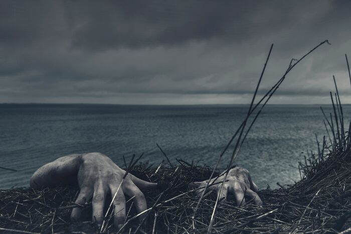 Hands emerging from dark soil near a body of water under a stormy sky, illustrating bizarre historical events.