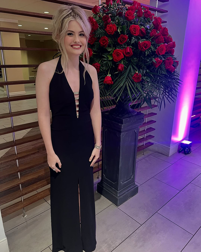 18-year-old Anna Nicole Smith look-alike wearing her mom's black dress, smiling beside a large red rose arrangement.