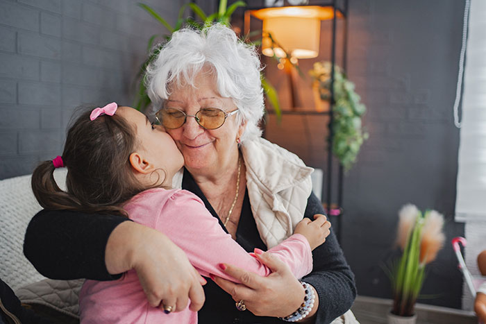 Grandmother and granddaughter hugging affectionately indoors, highlighting mom booked vacation and won&rsquo;t babysit kids.