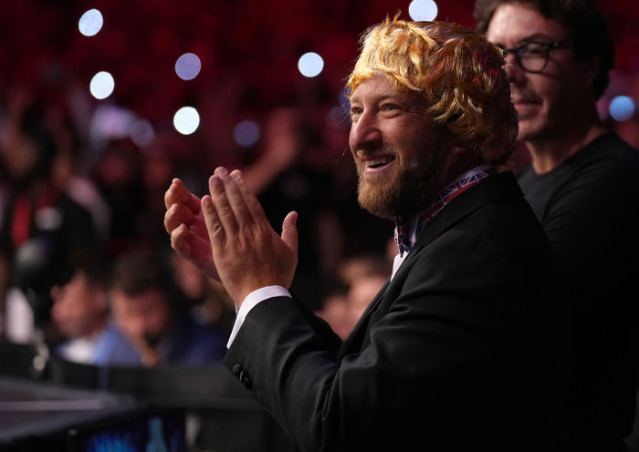 Dave Portnoy clapping, wearing a blonde wig and blazer in a lively, crowded event setting.