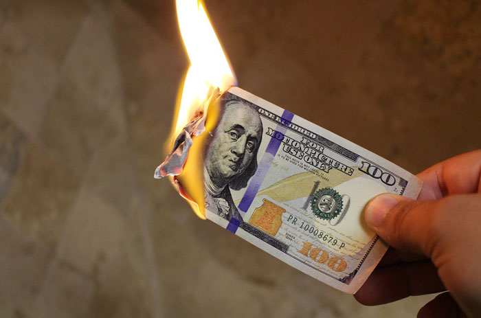 Burning one hundred dollar bill held by hand symbolizing loss related to Dave Portnoy net worth and fortune changes.