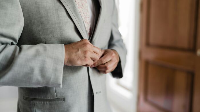 Man in a light gray suit buttoning jacket indoors, illustrating appalling facts people unaware in a professional setting