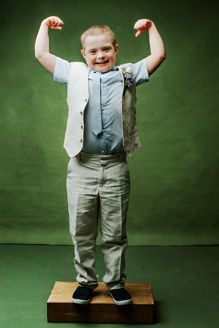 Young boy with Down syndrome in a suit flexing muscles confidently, symbolizing inclusion and strength.