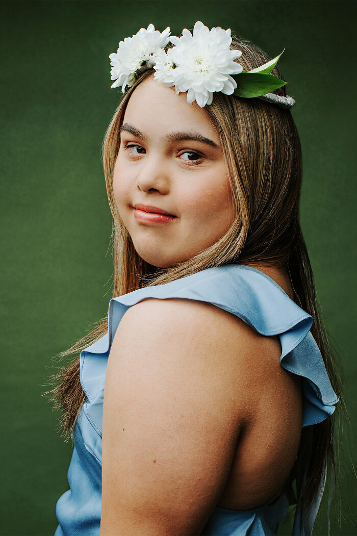 Young woman with Down syndrome wearing a blue dress and white flower crown, celebrating inclusion and positive representation.