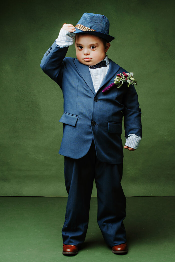 Young boy with Down syndrome in a blue suit and hat, showcasing inclusion and changing perceptions of Down syndrome.