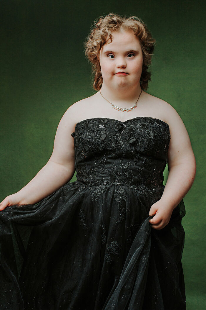 Young woman with Down syndrome wearing an elegant black dress, celebrating inclusion and diversity in a formal portrait setting.