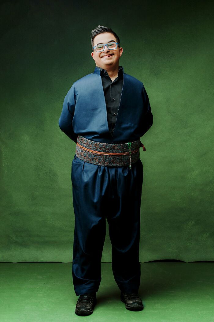 Young man with Down Syndrome smiling, wearing traditional clothing against a green backdrop, celebrating inclusion.