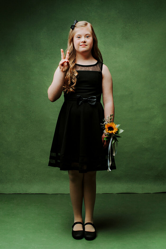 Young girl with Down syndrome in a black dress holding a sunflower, symbolizing inclusion and changing perceptions.