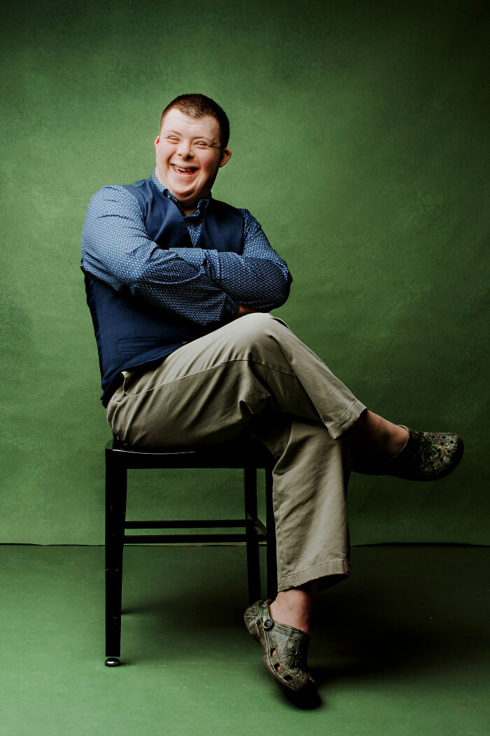 Smiling young man with Down syndrome sitting confidently on a chair, promoting inclusion and changing perceptions.