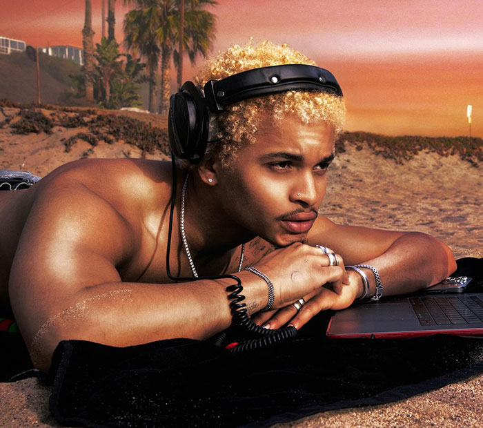 Young man with blonde curly hair wearing headphones, lying on the beach at sunset, focused on a laptop nearby. Young man with blonde curly hair wearing headphones, lying on the beach at sunset, focused on a laptop nearby.