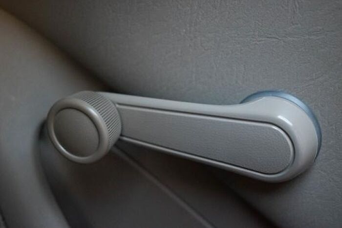 Manual car window crank handle inside a vehicle, evoking nostalgic cringey nineties fashions we left behind.
