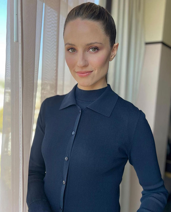 Former Glee star Dianna Agron posing indoors, wearing a navy blue top, showcasing her new accent and style.