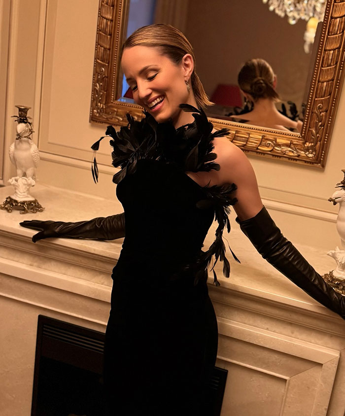 Former Glee star Dianna Agron wearing a black feathered dress and gloves, smiling beside a marble fireplace. Former Glee star Dianna Agron wearing a black feathered dress and gloves, smiling beside a marble fireplace.