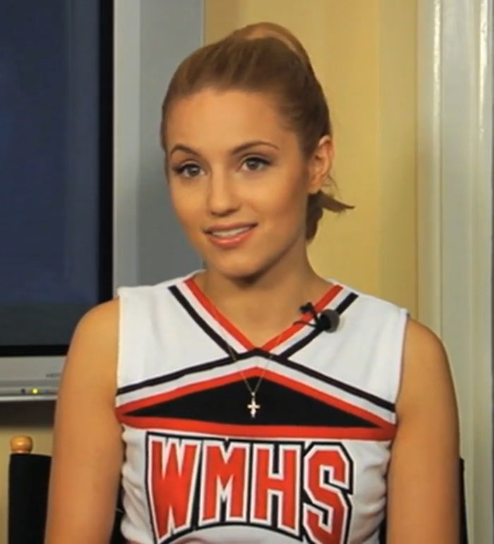 Former Glee star Dianna Agron wearing a WMHS cheerleader outfit, smiling during an interview about her new accent.