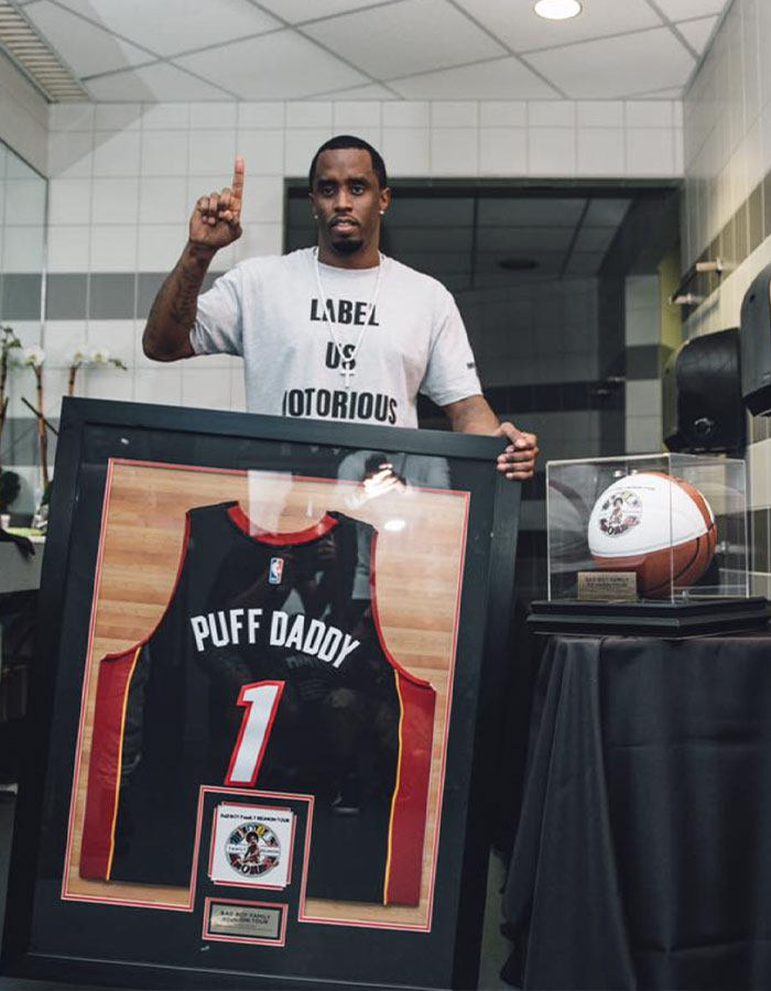 Man holding framed Puff Daddy basketball jersey and basketball display case, related to Diddy trial Miami mansion raid items.