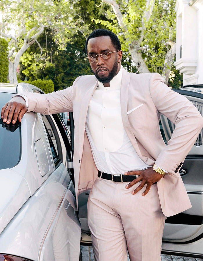 Diddy posing outside a luxury car wearing a light suit, linked to Miami mansion raid and disturbing items in trial.