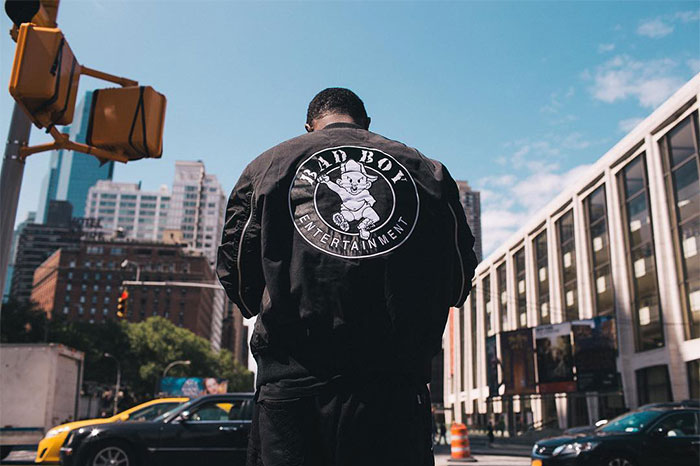 Diddy wearing a Bad Boy Entertainment jacket standing in the city, symbolizing Diddy's net worth and legal trouble impact.
