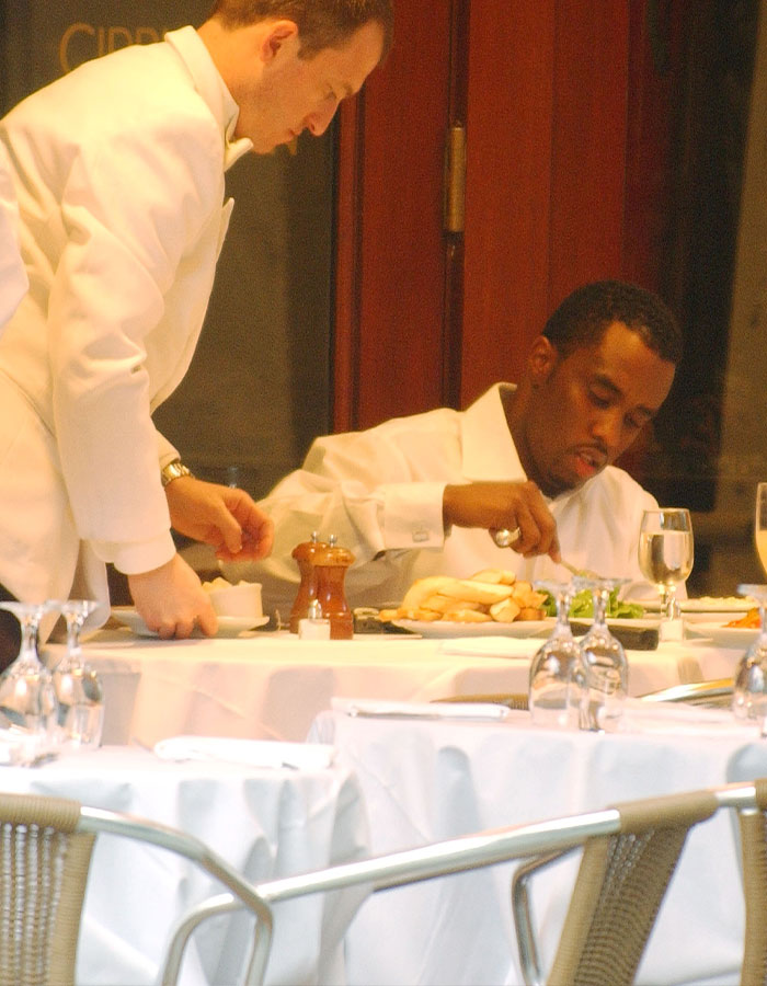 Man resembling Diddy eating at a table while waiter serves, highlighting disgust and revolting eating habits revealed by staff. Man resembling Diddy eating at a table while waiter serves, highlighting disgust and revolting eating habits revealed by staff.