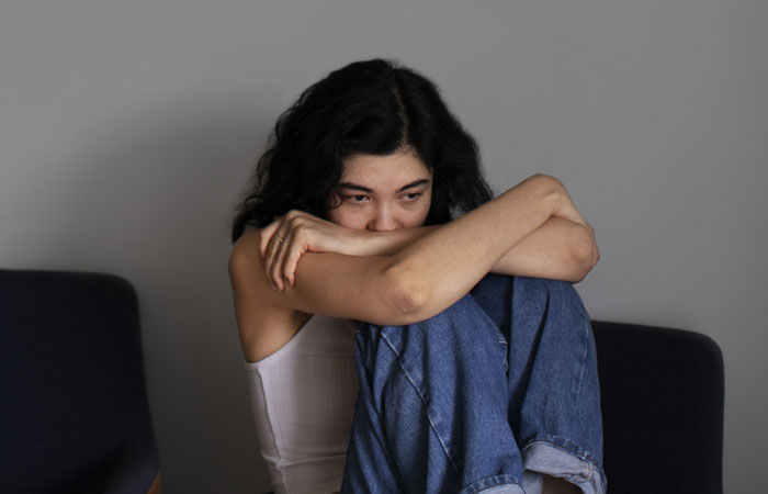 Sad young woman sitting curled up on a chair, reflecting on cousin betrayal and dealing with emotional forgiveness.